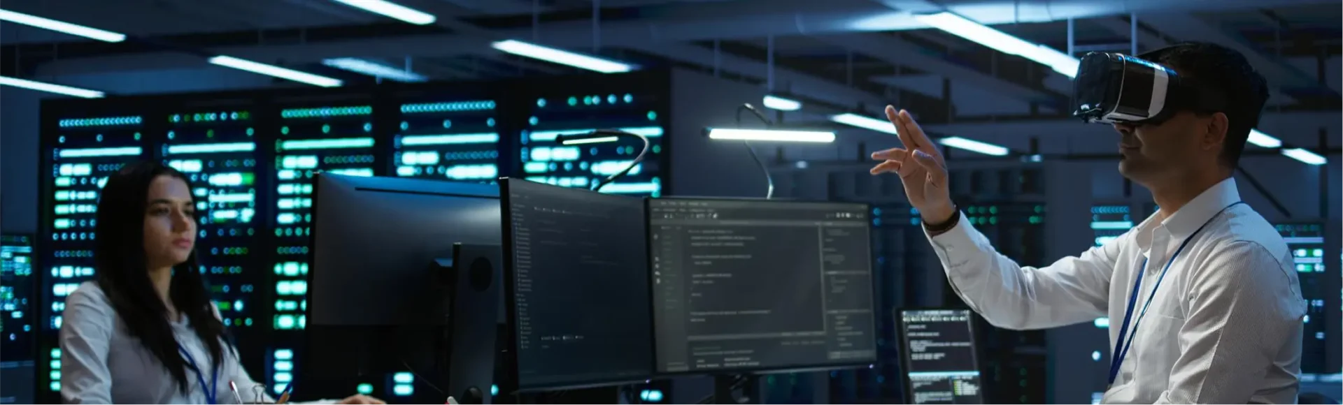 A man and woman wearing VR headsets, engaged with a computer screen in a modern workspace.